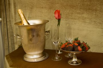 A bottle of champagne in an ice bucket, two empty champagne flutes, a single red rose, and a glass plate of chocolate-covered strawberries on a table—just one example of the romantic touches you’ll discover with our South Carolina vacation packages.