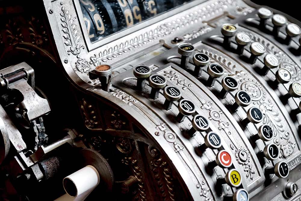 Close-up of an ornate, vintage metal cash register with round keys, decorative engravings, and a visible paper roll on the side—an intriguing piece you might spot while exploring unique things to do in Latta and Florence SC.